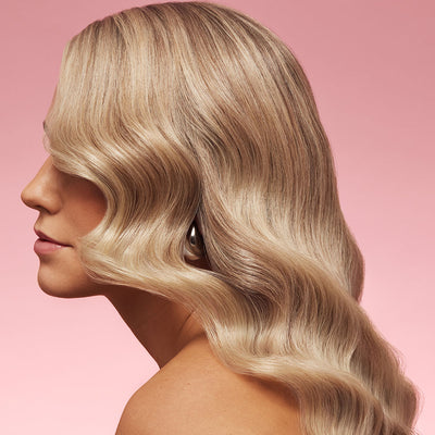 Side profile of a person with wavy blonde hair against a pink background